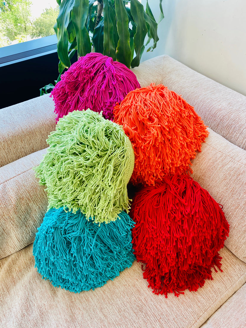 A pile of Crochet Joni Pillows by Huldra of Norway in different colors on the corner of a couch.