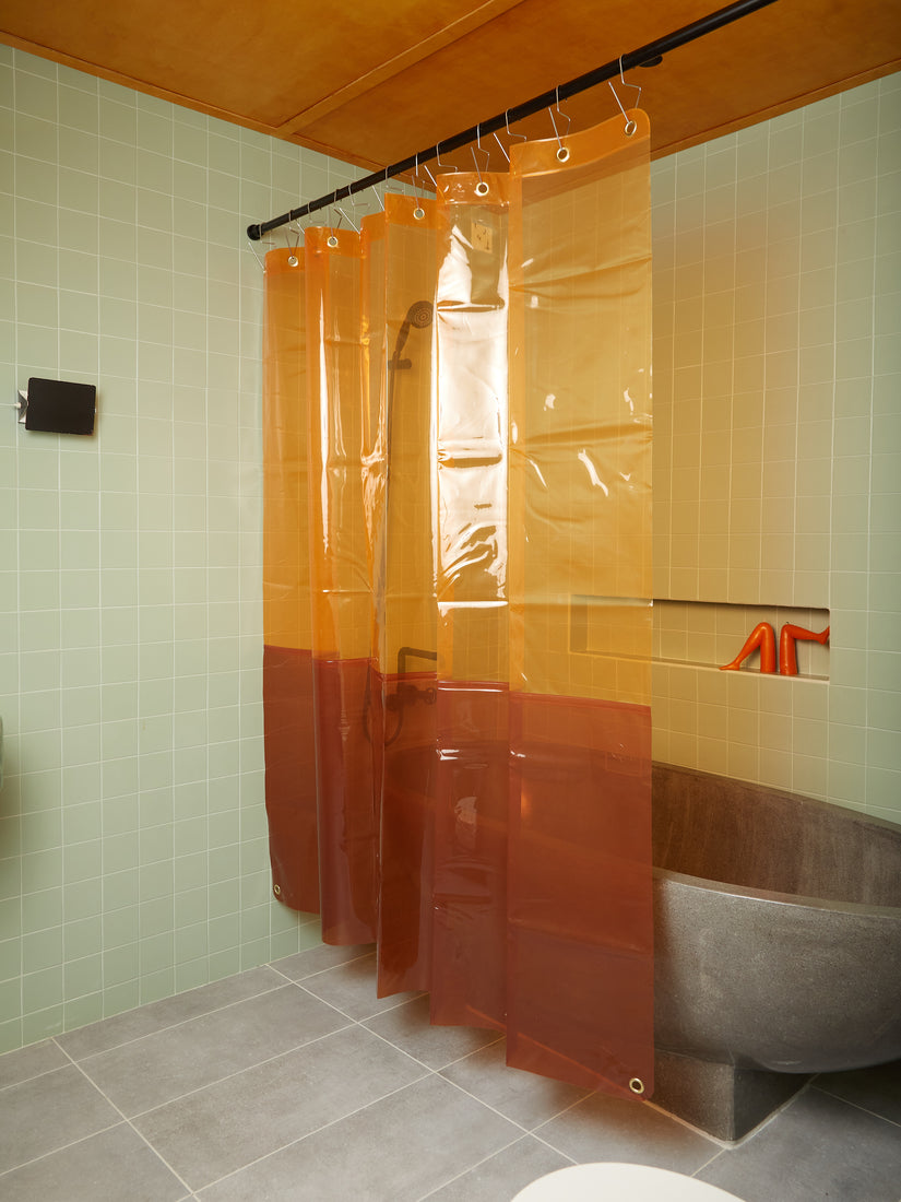 An orange top amber bottom Orient Sun Shower curtain hung in front of a rounded stone bathtub.