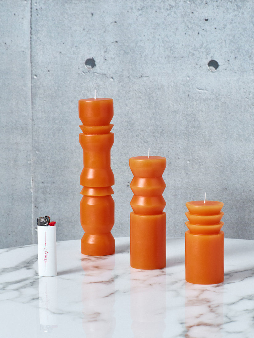 Orange Totem Candles in small, medium, and large next to a white Coming Soon lighter.