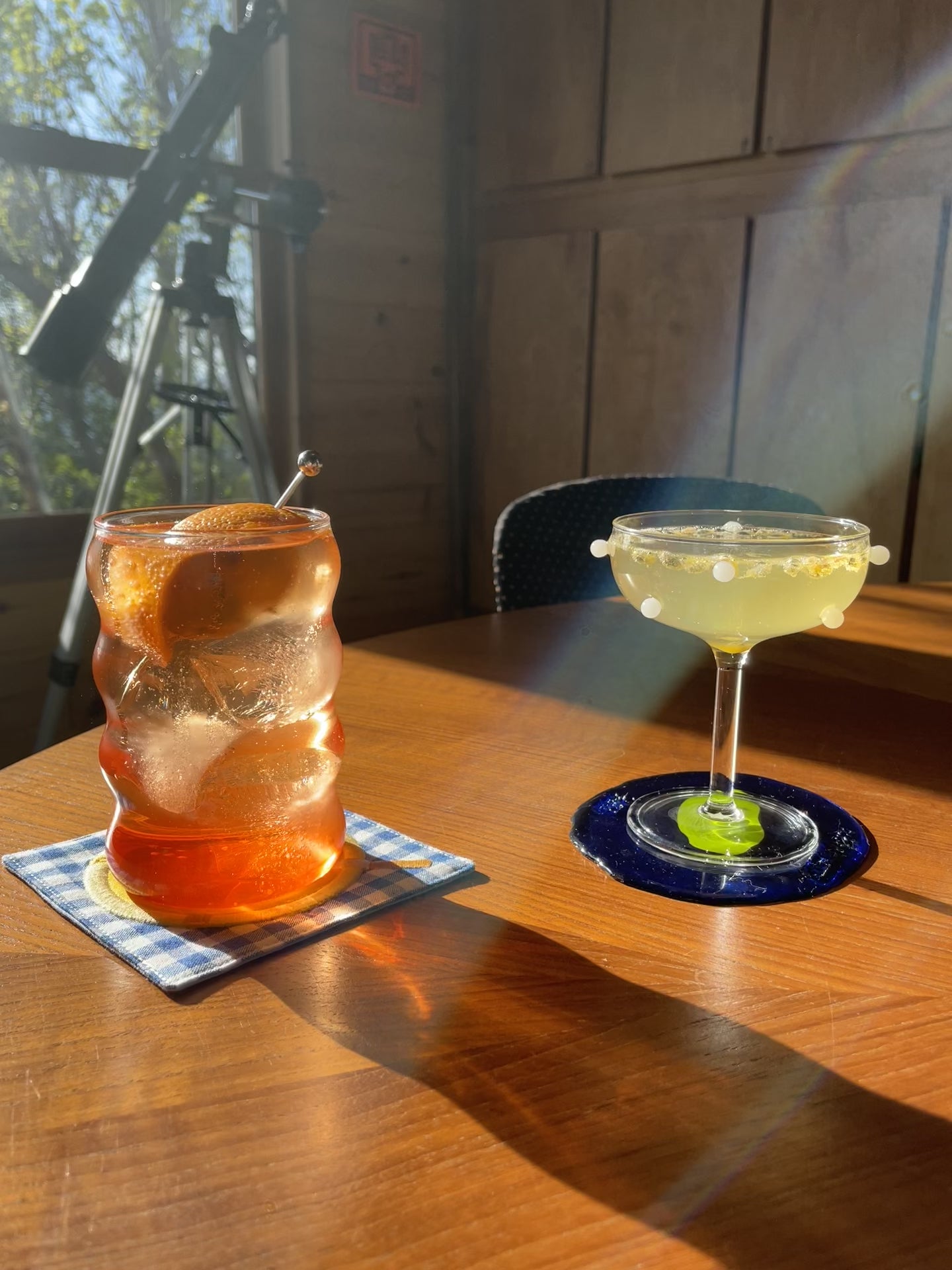 A cocktail lightly bubbling inside a white dot coupe on a sunny wooden table.